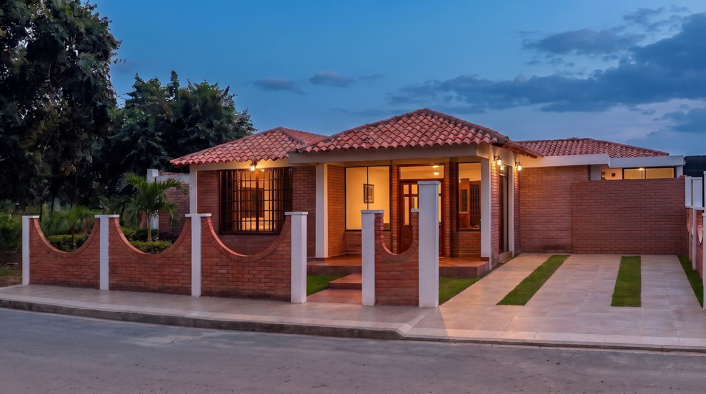 Vista de anochecer de la vivienda con iluminación cálida en el pórtico y las ventanas